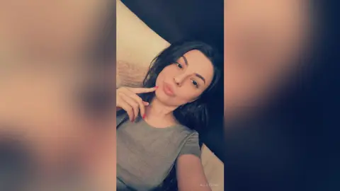 Smiling young woman in a casual grey t-shirt relaxing on a white sofa in a cozy indoor setting.