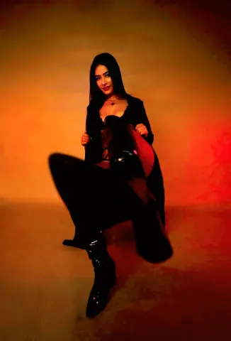 Elegant woman in a black outfit sitting against a warm red and orange sunset background.
