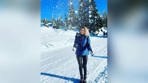 Smiling woman in a blue winter jacket playing in the snow at a sunny mountain ski resort.