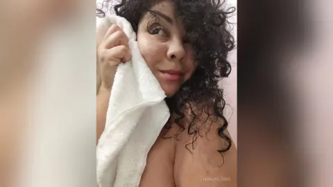 Smiling woman with curly dark hair wrapped in a white towel in a bright, cozy indoor setting.