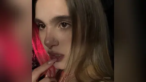 Close-up portrait of a young woman with long hair and nose ring in moody, warm lighting.