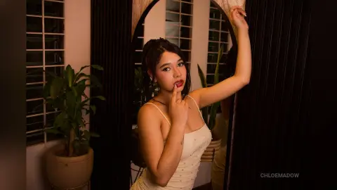 Young woman in a white slip dress posing thoughtfully in a warm, moody indoor setting with plants.