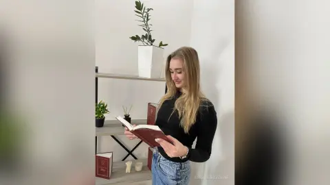 Blonde woman in a black long-sleeve shirt reading a book in a bright, minimalist modern living room.