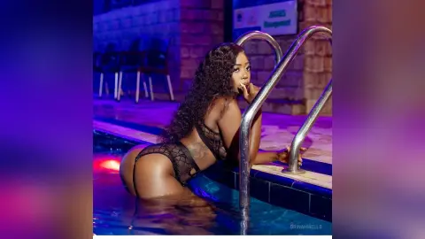 Glamorous woman in black lace swimwear relaxing in a luxury swimming pool under moody purple lighting.