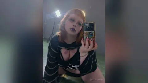 Redheaded woman in a black striped crop top taking a moody selfie in a studio setting.