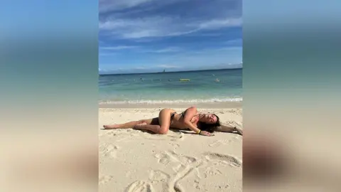 Fit woman in black bikini relaxing on a sunny tropical beach under a blue sky.