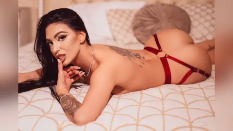 Iza — Tattooed woman in red lingerie lying on a white patterned bed in a soft, intimate mood.