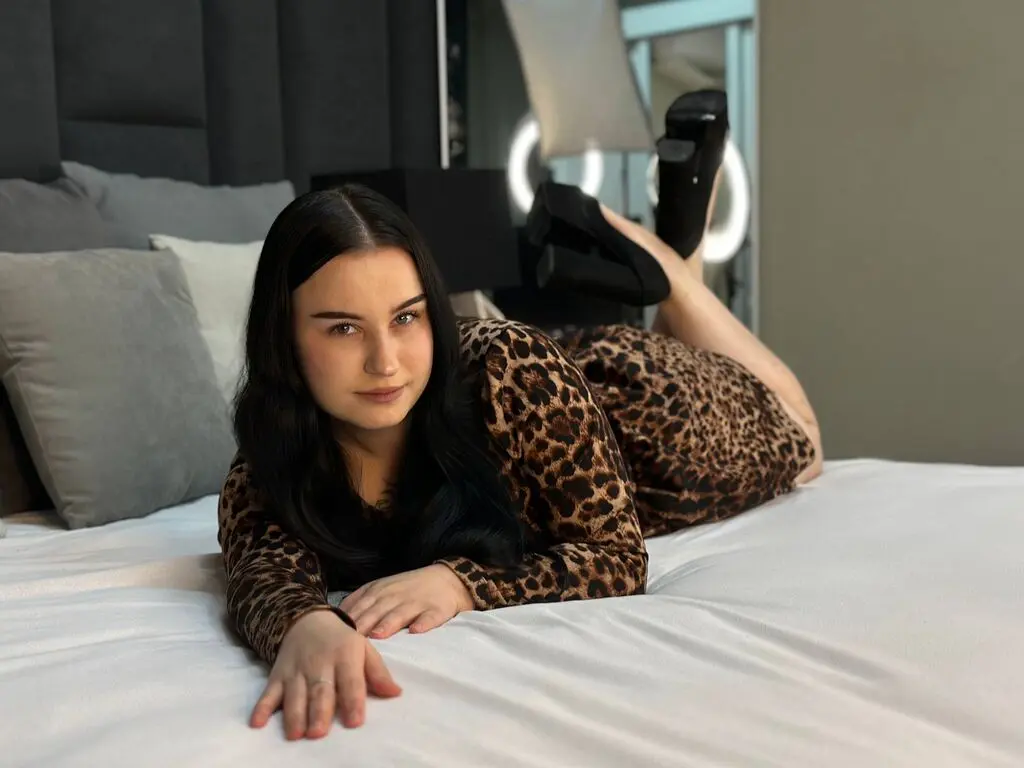 Young woman in a leopard print dress relaxing on a white bed in a cozy bedroom setting.