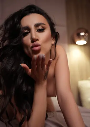 Beautiful woman with long wavy hair blowing a kiss in a warm, cozy indoor setting.