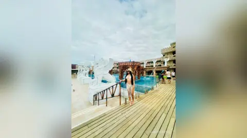 Stylish woman in a bikini and sun hat relaxing by a luxury resort pool with white lion statues.