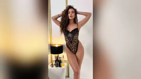 Brunette woman in a black lace leopard print bodysuit posing in a bright, modern room.