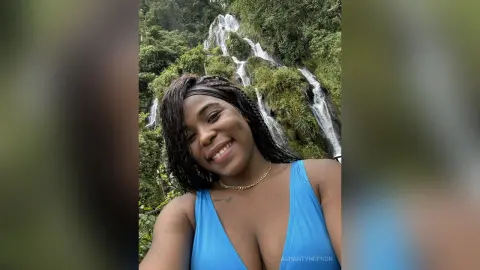 Smiling woman in a blue swimsuit enjoying a lush tropical waterfall landscape.