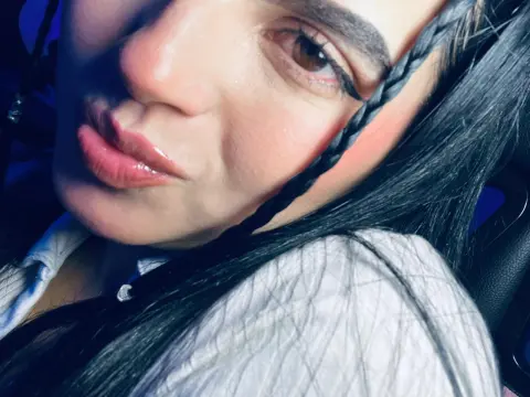 Close-up portrait of a woman with long dark hair and braids wearing a white shirt in moody blue lighting.