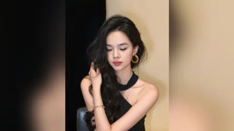 Elegant woman in a black halter top and gold hoop earrings posing with a soft, moody expression.