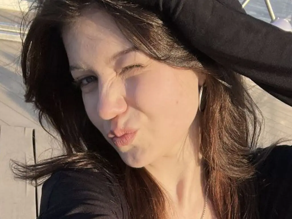 Smiling young woman in a black top making a playful face on a sunny wooden deck.