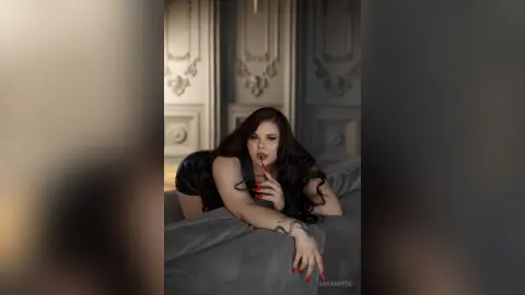 Elegant woman in a black dress lounging on a sofa in a moody, classic interior setting.