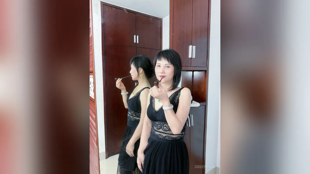GreenHua — GreenHua wears a black lace dress and holds a smoking pipe while standing in front of a dark wood wardrobe.