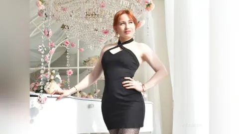 Elegant woman in a black halter dress posing by a white piano under a crystal chandelier in a bright room.