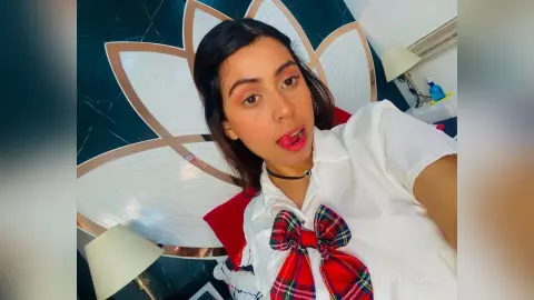 Young woman in a white collared shirt and red plaid bow tie posing in front of a decorative lotus mirror.