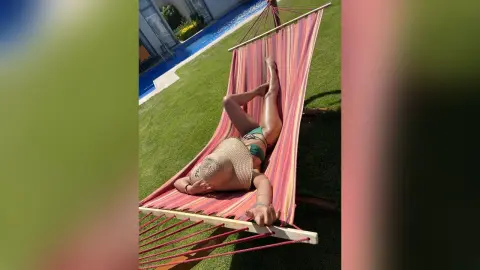 NicoleBella reclines in a pink and red striped hammock, wearing a green bikini and a straw sun hat.
