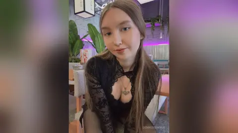 Young woman in a black lace long-sleeve top and necklace sitting in a bright modern cafe.