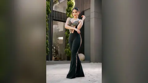Elegant woman in a black lace bodysuit and flared trousers posing in a modern outdoor courtyard.