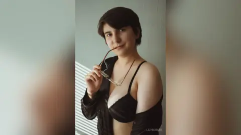 Smiling young woman in a black bra and open shirt posing in soft natural light for a moody portrait.