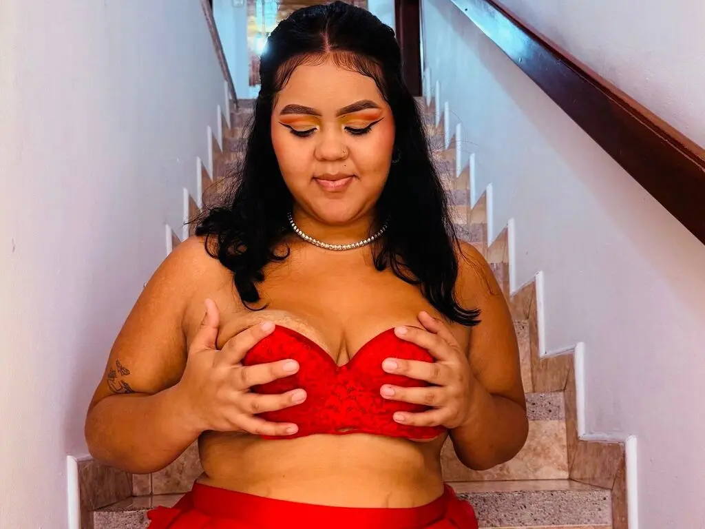 Young woman in a red lace bra and skirt sitting on stairs with warm, glowing makeup.