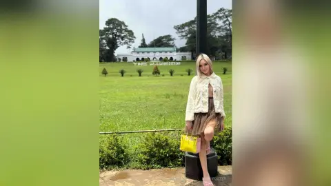 Stylish woman in a white fuzzy jacket and brown skirt posing with a yellow handbag in a lush green park.