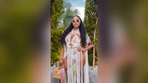 Stylish woman in a white cutout fringe maxi dress and sunglasses posing outdoors in a lush garden setting.