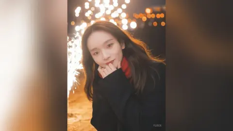 Smiling woman in a black coat and red scarf enjoying a festive night with glowing bokeh lights.