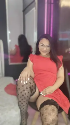 Smiling woman in a red dress and polka dot tights sitting in a modern room with soft lighting.