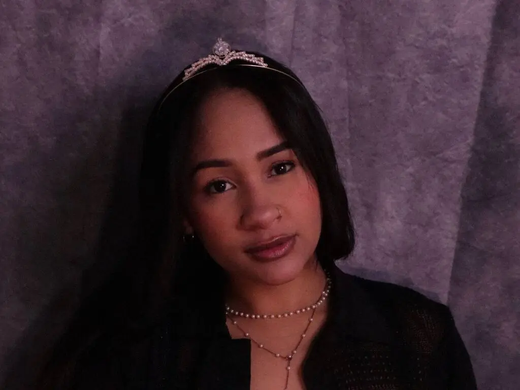 Elegant woman in a black outfit and silver tiara posing against a textured purple backdrop with a moody vibe.