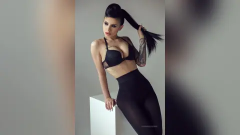 Athletic woman in black sports bra and leggings posing confidently in a minimalist studio setting.