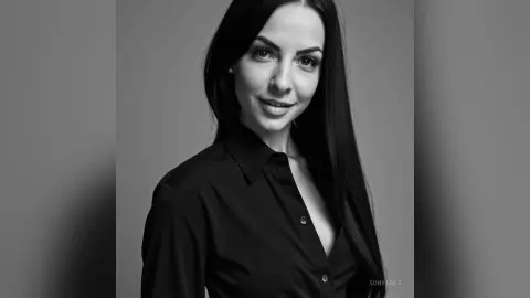 Smiling young woman with long dark hair wearing a black button-down shirt in a minimalist black and white portrait.