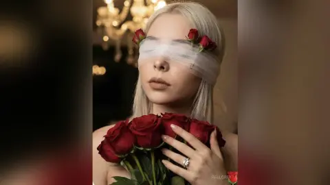 Blonde woman with rose flower blindfold holding red roses in a moody, romantic indoor setting.