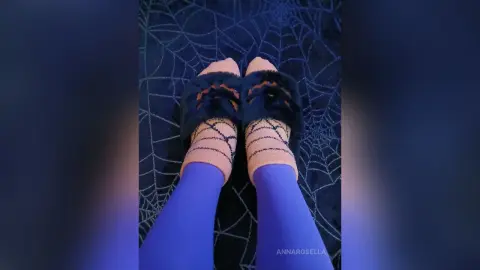 Person wearing cozy orange spiderweb socks and fuzzy black slippers on a spooky dark spiderweb rug.