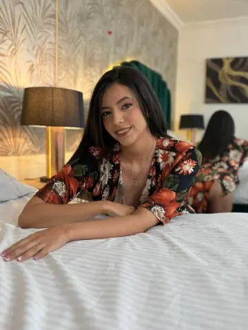 Smiling young woman in a floral print robe relaxing on a white bed in a modern bedroom.