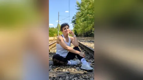 JaneHope — JaneHope sits on railroad tracks wearing a white tank top and black leggings.