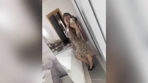 Woman in a brown zebra print mini dress taking a mirror selfie in a bright modern bedroom.