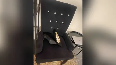 Elegant black high heel pumps resting on a stylish black velvet studded accent chair in a modern room.