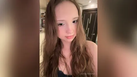 LaritaLudemann looks at the camera with long brown hair and a black lace top.