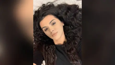 Young woman with long curly dark hair wearing a black top, relaxing with a serene expression.