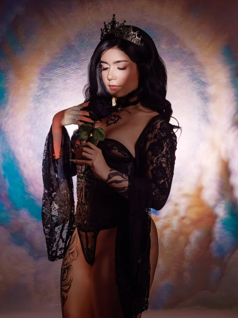 Young woman with black bangs and dramatic eye makeup posing in a moody, dark setting.