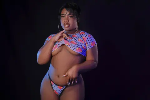 Confident woman in a colorful patterned bikini set posing against a dark studio background.
