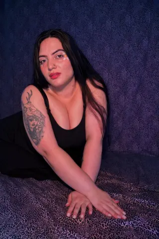 Woman in a black tank top sitting against a dark leopard print background with a moody aesthetic.