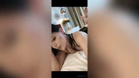 AnnaliseAshton — AnnaliseAshton lies on a white bed in black lingerie, looking into the camera with long dark hair.
