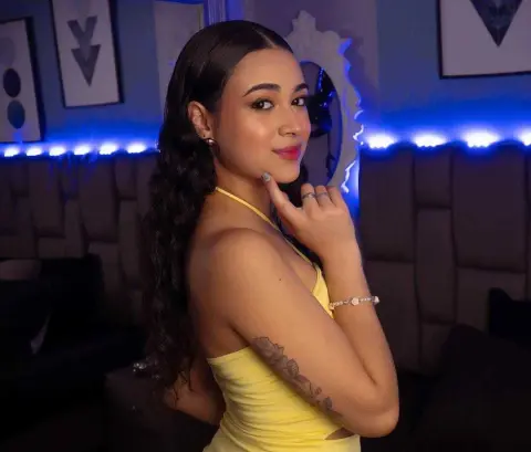 Smiling young woman in a yellow halter top posing in a room with blue neon mood lighting.