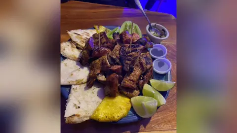 Grilled chicken skewers served with pita bread and lime wedges on a blue plate in a dimly lit restaurant.