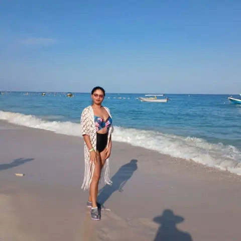 VictoriaaBailey stands on a sunny beach wearing a patterned bikini top, black bottoms, and a white crochet cover-up.